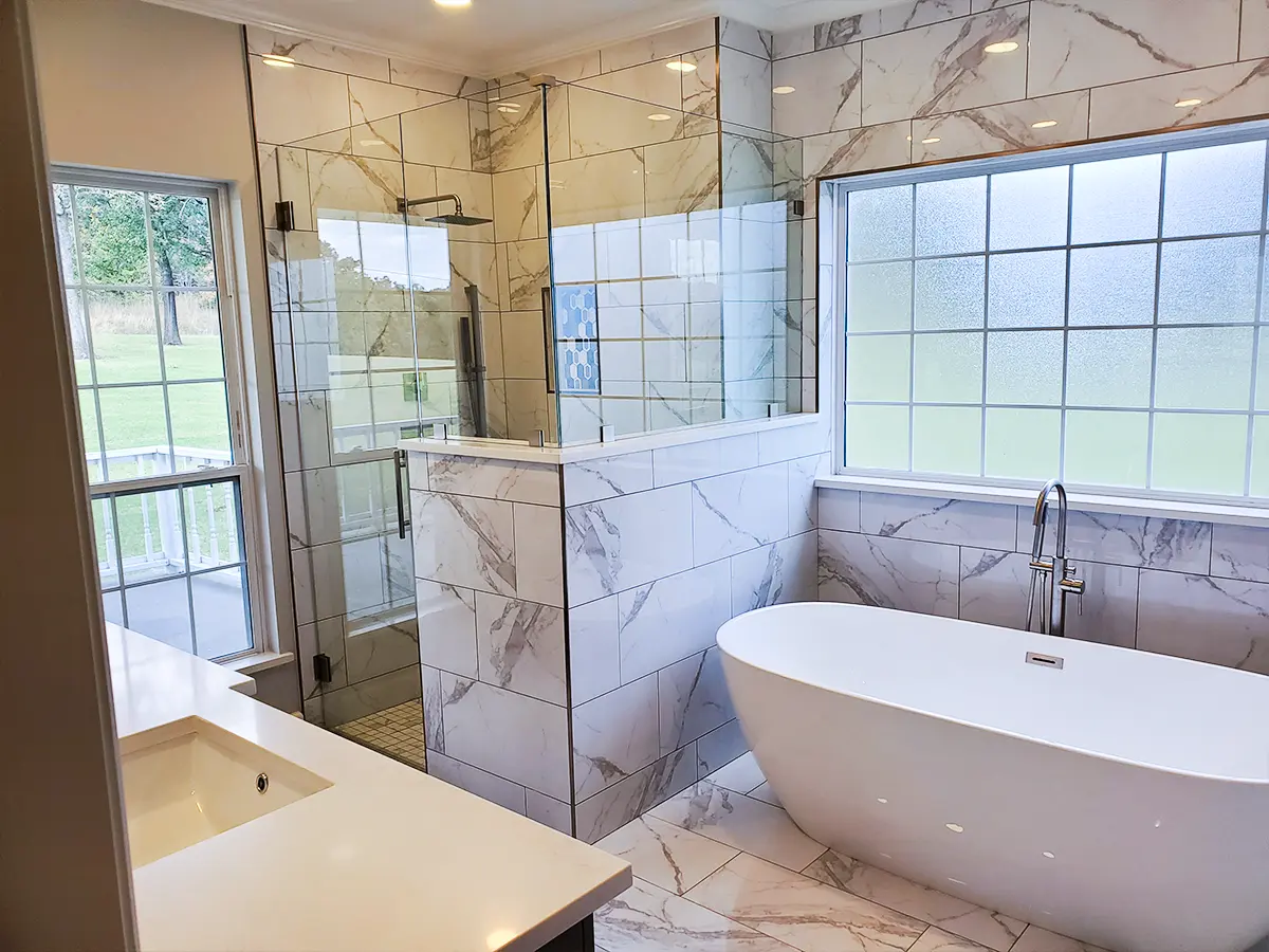 A beautiful bathroom renovation with porcelain tile floor and walls, framed shower, and freestanding tub