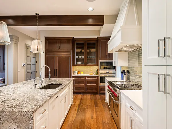 A kitchen with a granite countertop, white and brown kitchen cabinets, and wood floors