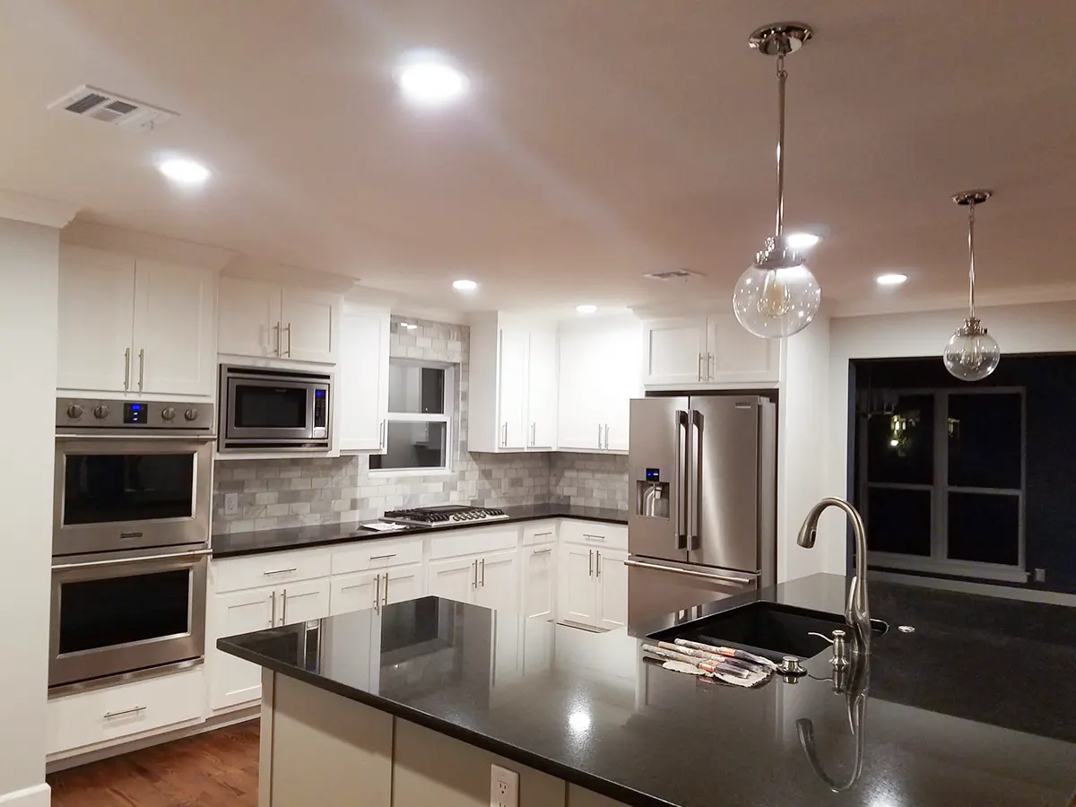 A large kitchen with white kitchen cabinets, black countertop, and silver appliances