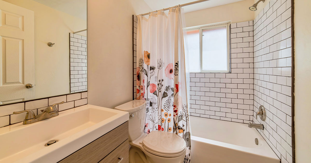 A cozy bathroom featuring a floral shower curtain, white subway tiles, a vanity with a large mirror, and modern fixtures.