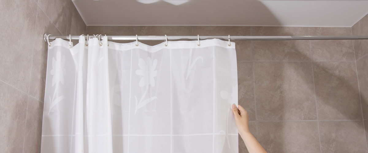 A minimalist bathroom featuring a plain white shower curtain being pulled closed, with beige tiled walls and modern fixtures.