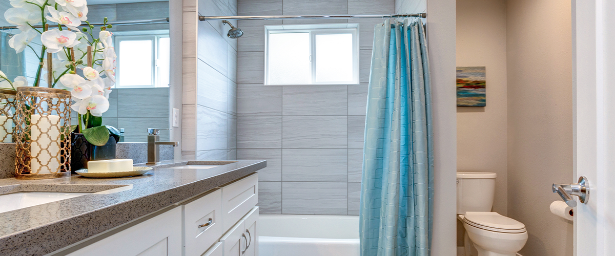 A modern bathroom with a light blue shower curtain, white vanity with a gray countertop, and decorative elements