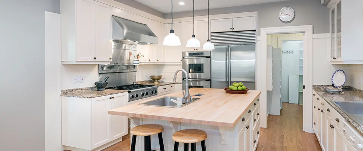 Modern white kitchen remodeling in Sand Springs, with stainless steel appliances, large island with butcher block top, pendant lighting, and walk-in pantry.